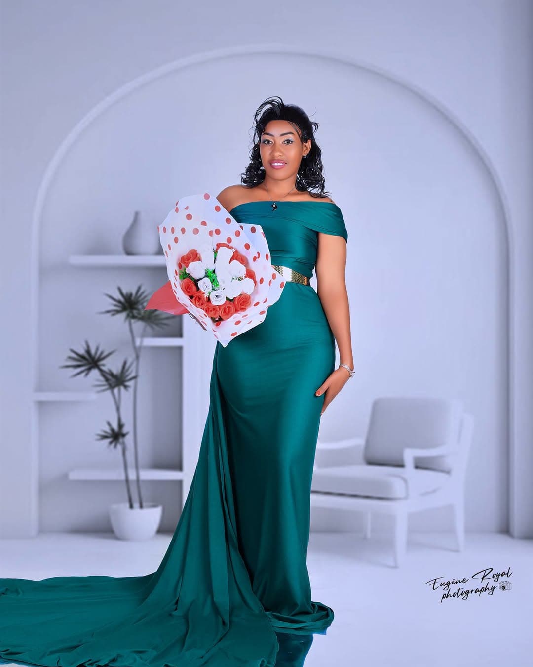 Woman in an emerald satin gown holding a bouquet in a white arched studio set