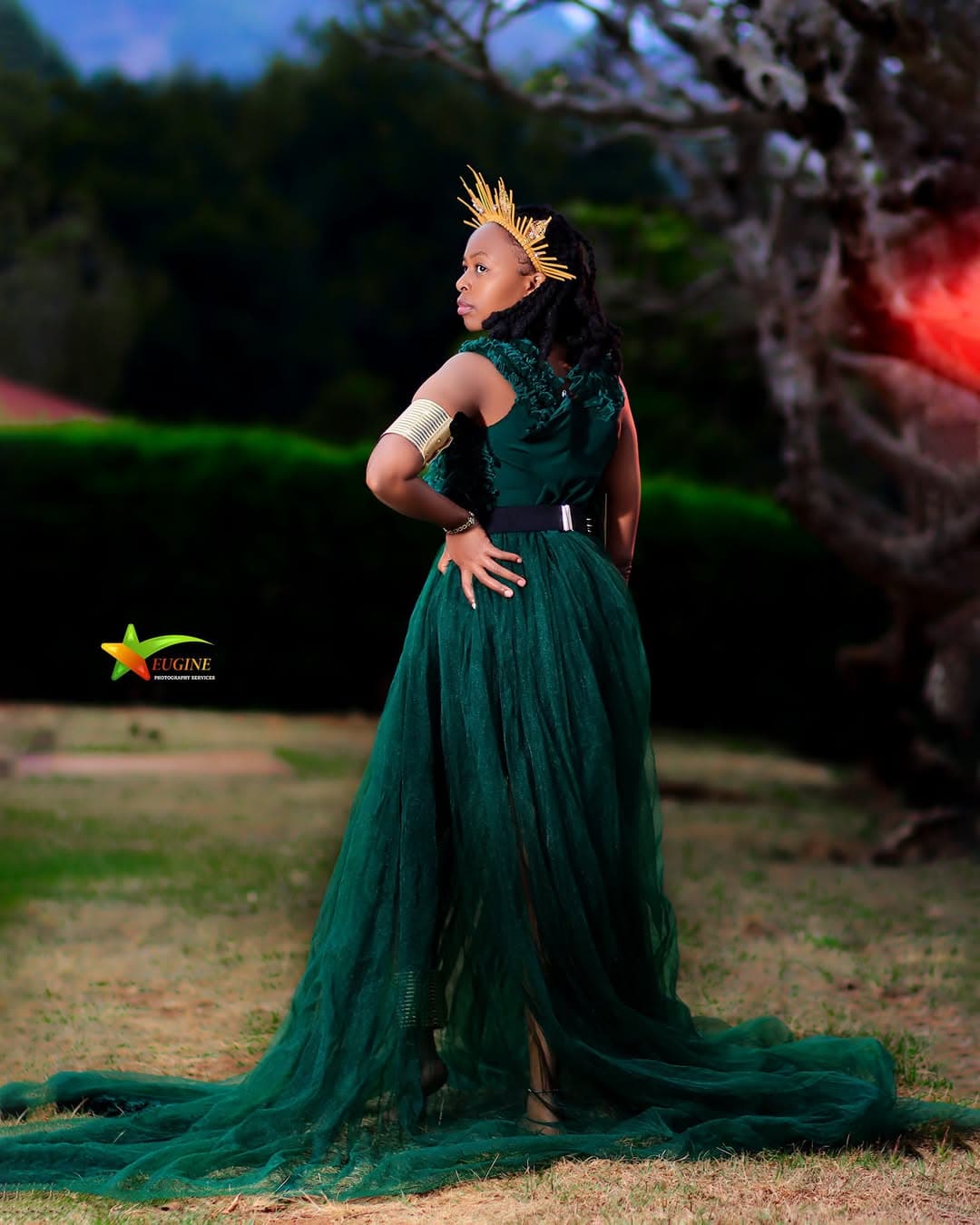 Birthday portrait of a woman in a green tulle gown and gold crown, looking over her shoulder in a garden