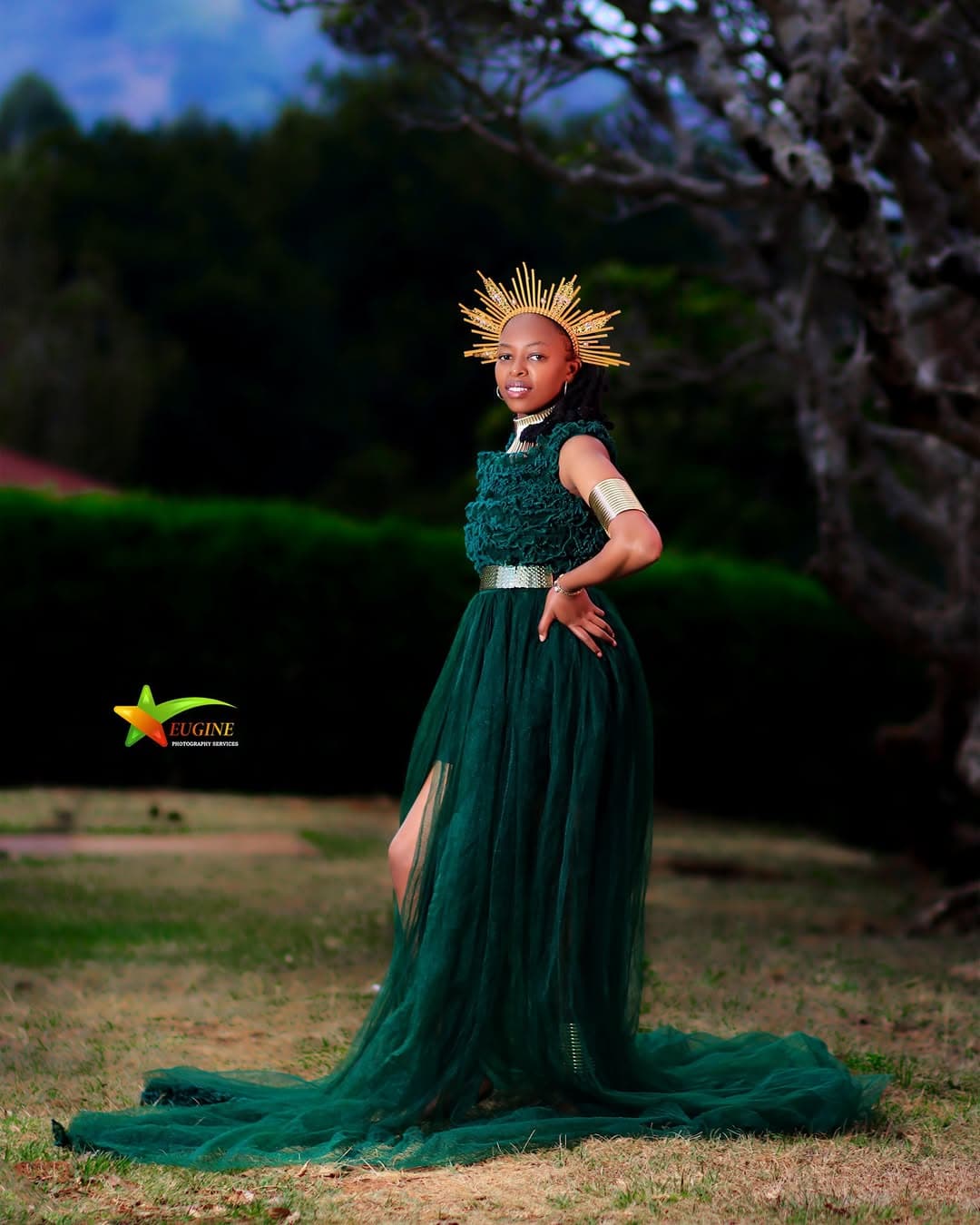Young woman in a green tulle gown and gold crown standing on a lawn