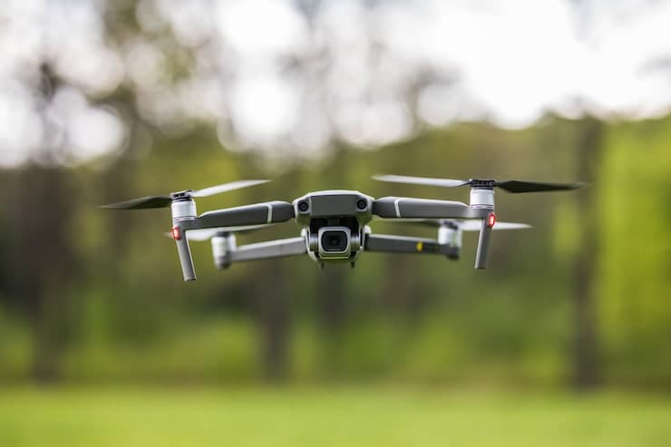 Grey camera drone hovering above a green park