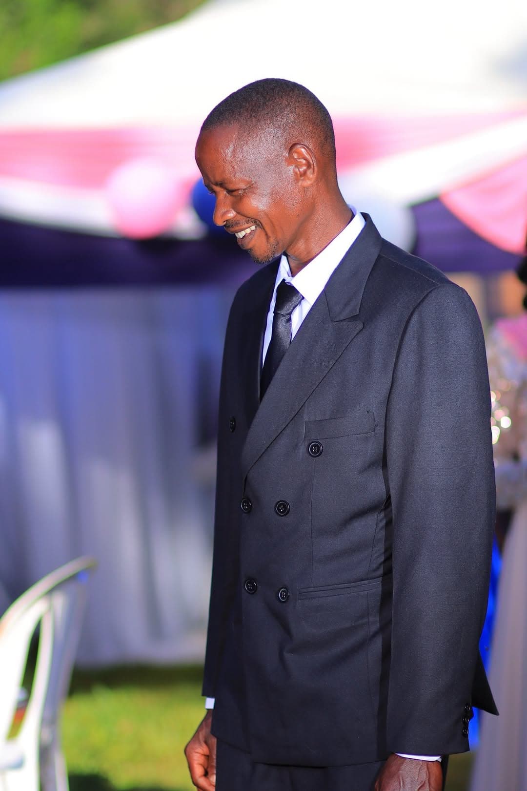 Groom laughing in a dark suit beside the reception tent