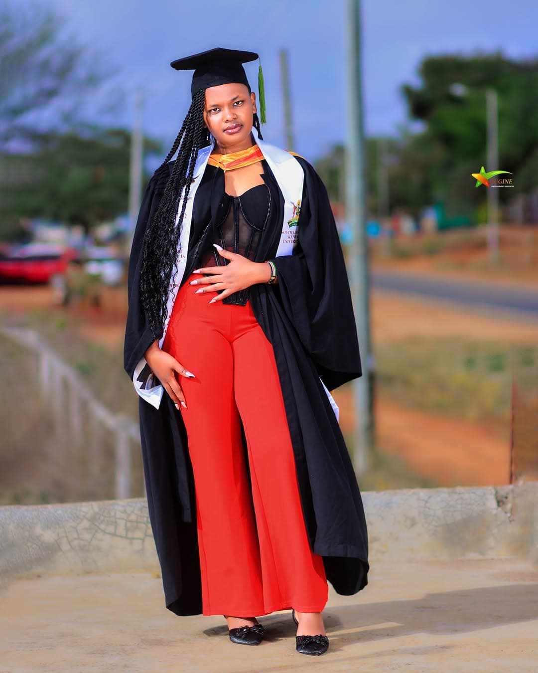 Graduate in a black gown and red trousers posing outdoors