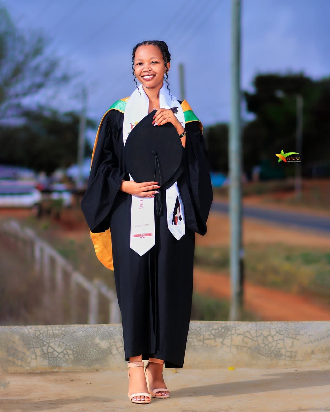 Smiling graduate in a black gown and stole holding her cap