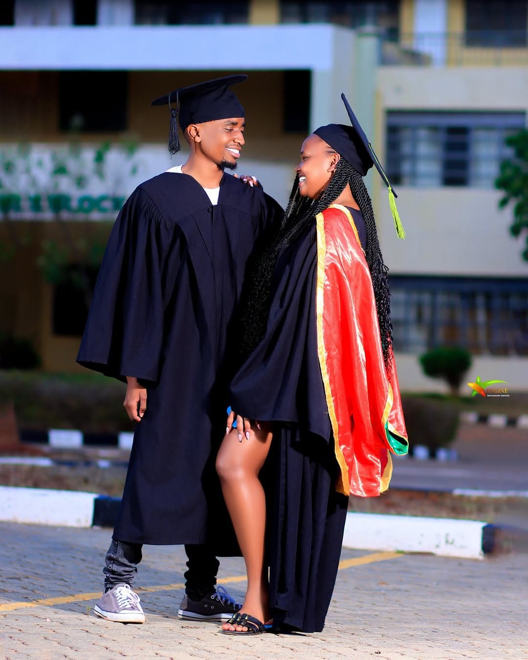 Two graduates in gowns and caps smiling at each other on campus
