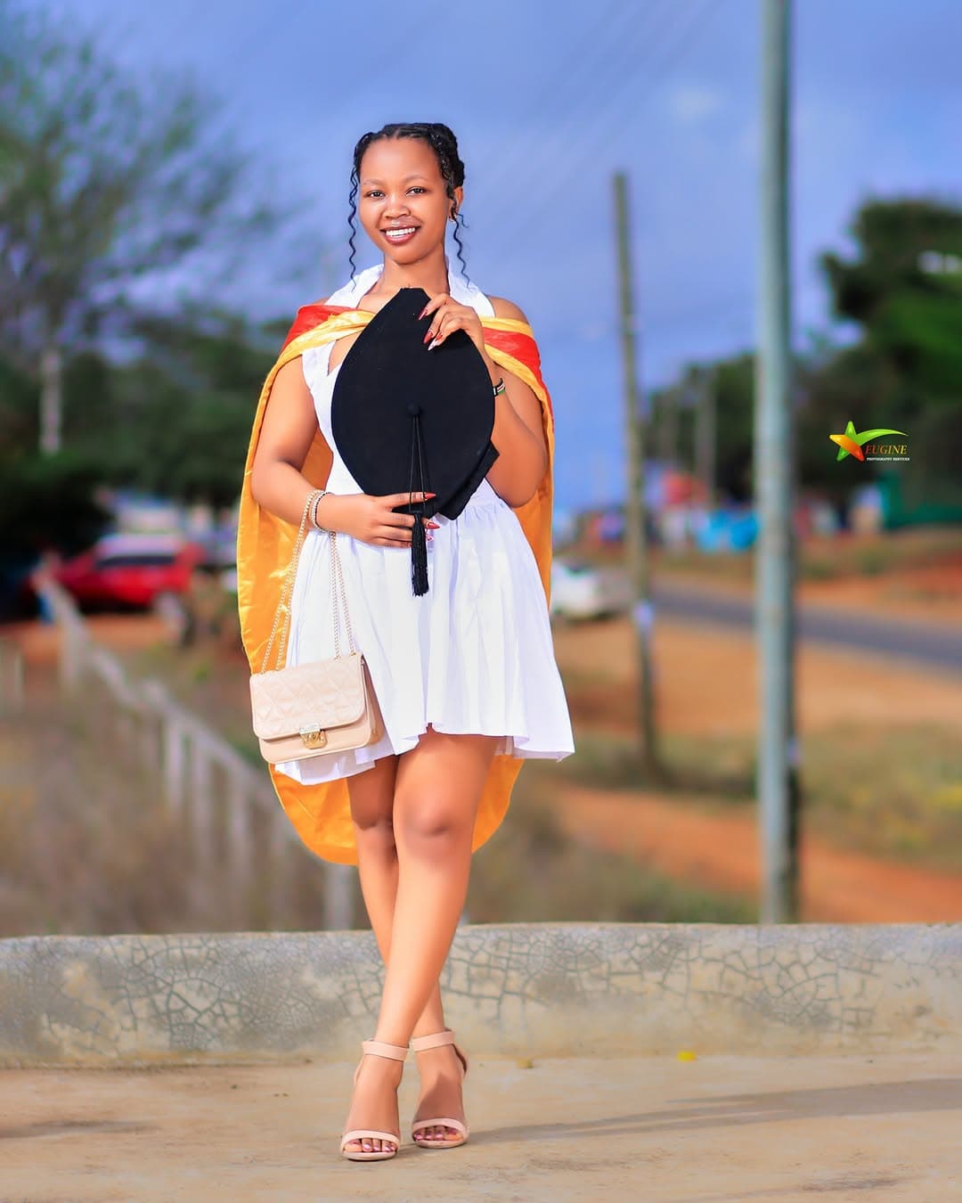 Graduate in a white dress and stole smiling with her cap
