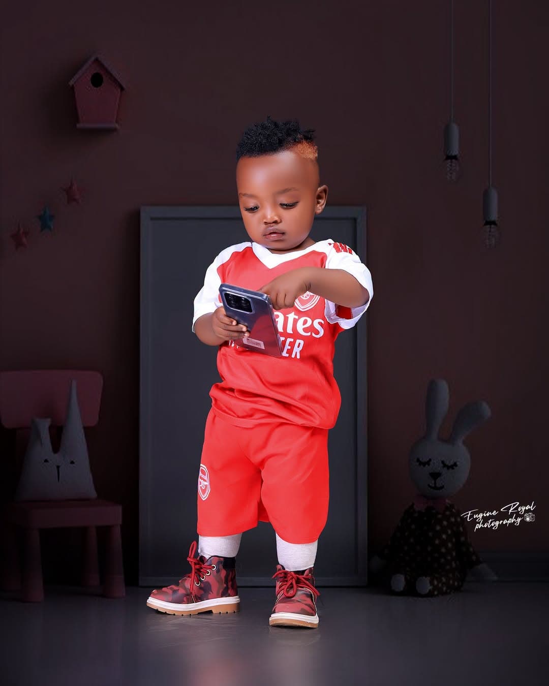 Toddler in a red football kit looking at a phone in a studio set