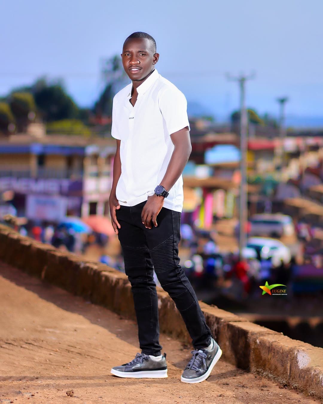 Man in a white shirt and black jeans posing above a town street