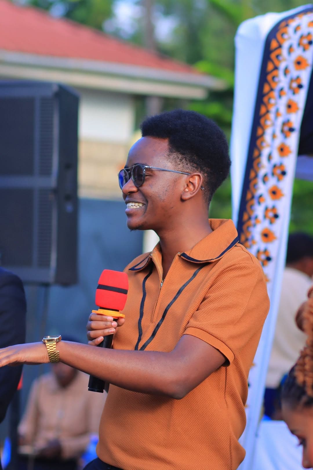 Smiling MC in a rust-coloured shirt speaking into a microphone