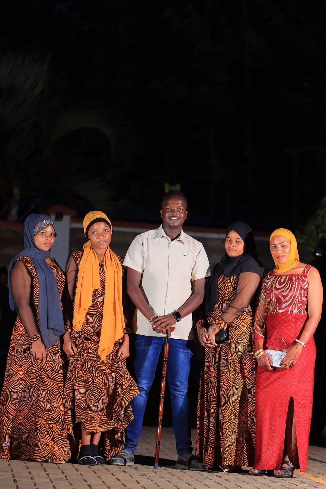 Women in printed dresses and headscarves posing with a guest at night