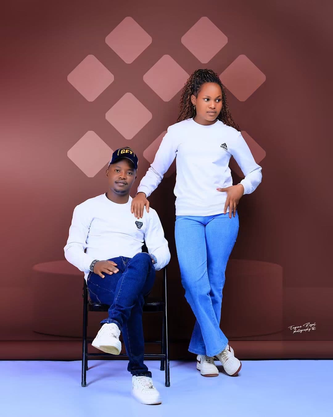 Couple in white tops and jeans posing on a terracotta studio set with a diamond-patterned wall