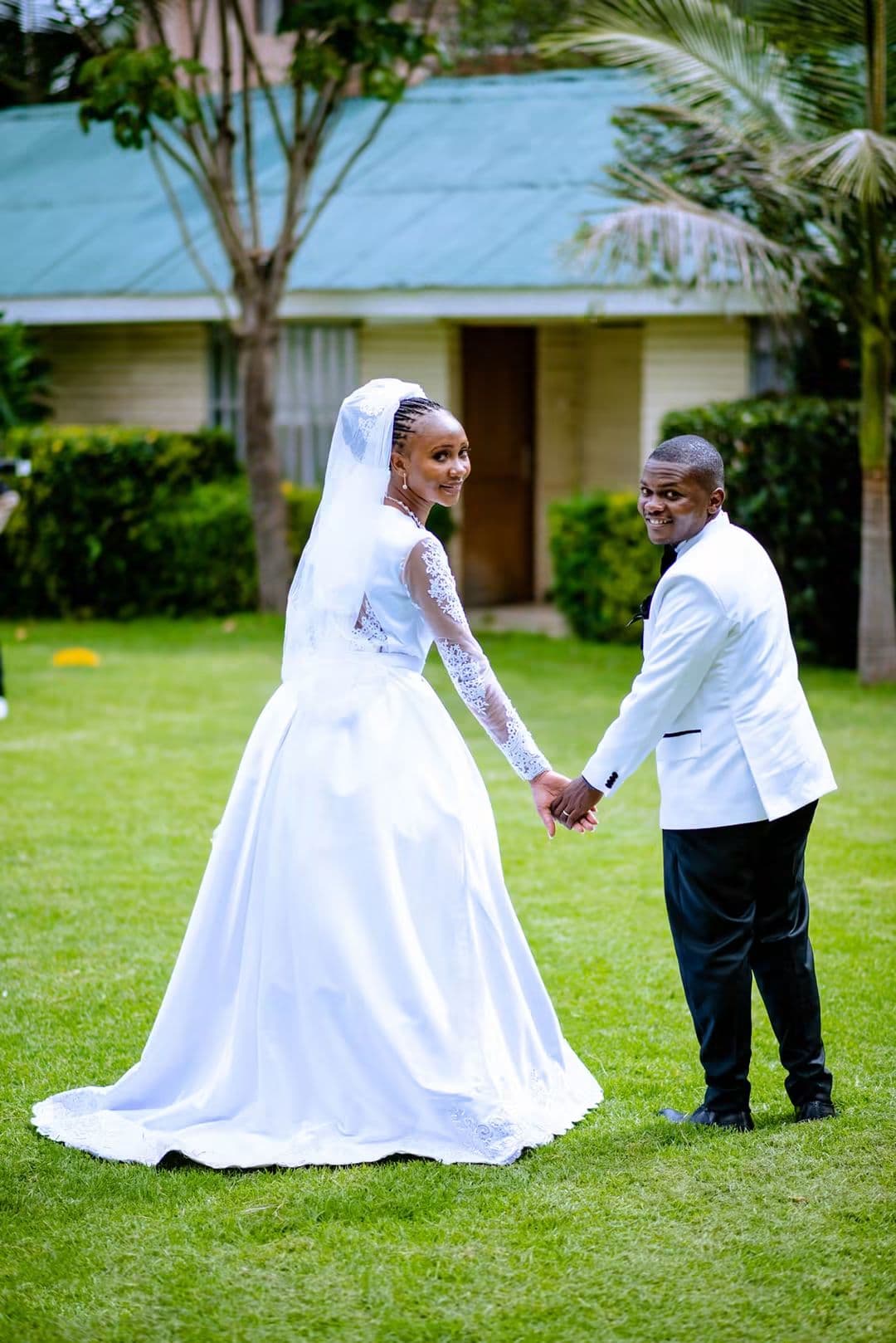 Bride and groom facing each other hand in hand on a garden lawn