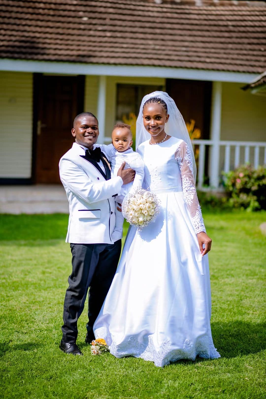 Groom holding a small child beside the bride on the lawn