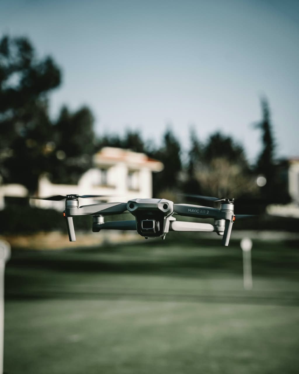Camera drone flying over a lawn with trees and a house behind