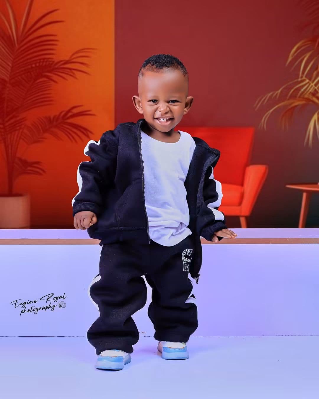 Laughing toddler in a black tracksuit standing in an orange studio set