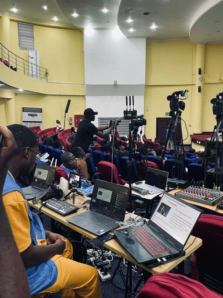 Crew streaming a hall event from a desk of laptops and a mixer, with cameras on tripods behind