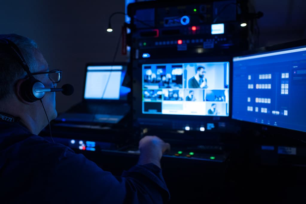 Broadcast operator in headphones at a live-production desk lit by monitors