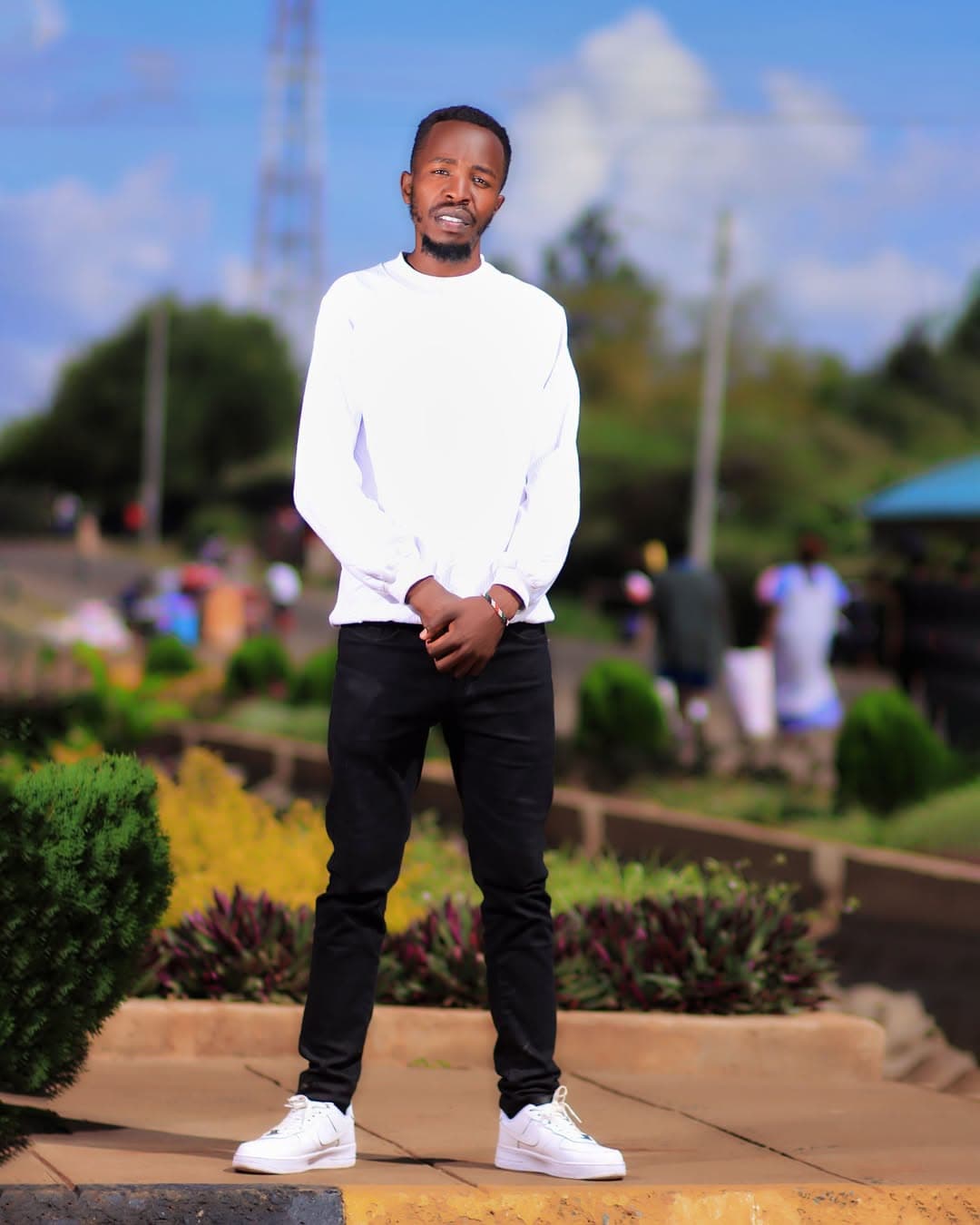 Man in a white sweater standing in a garden under a blue sky