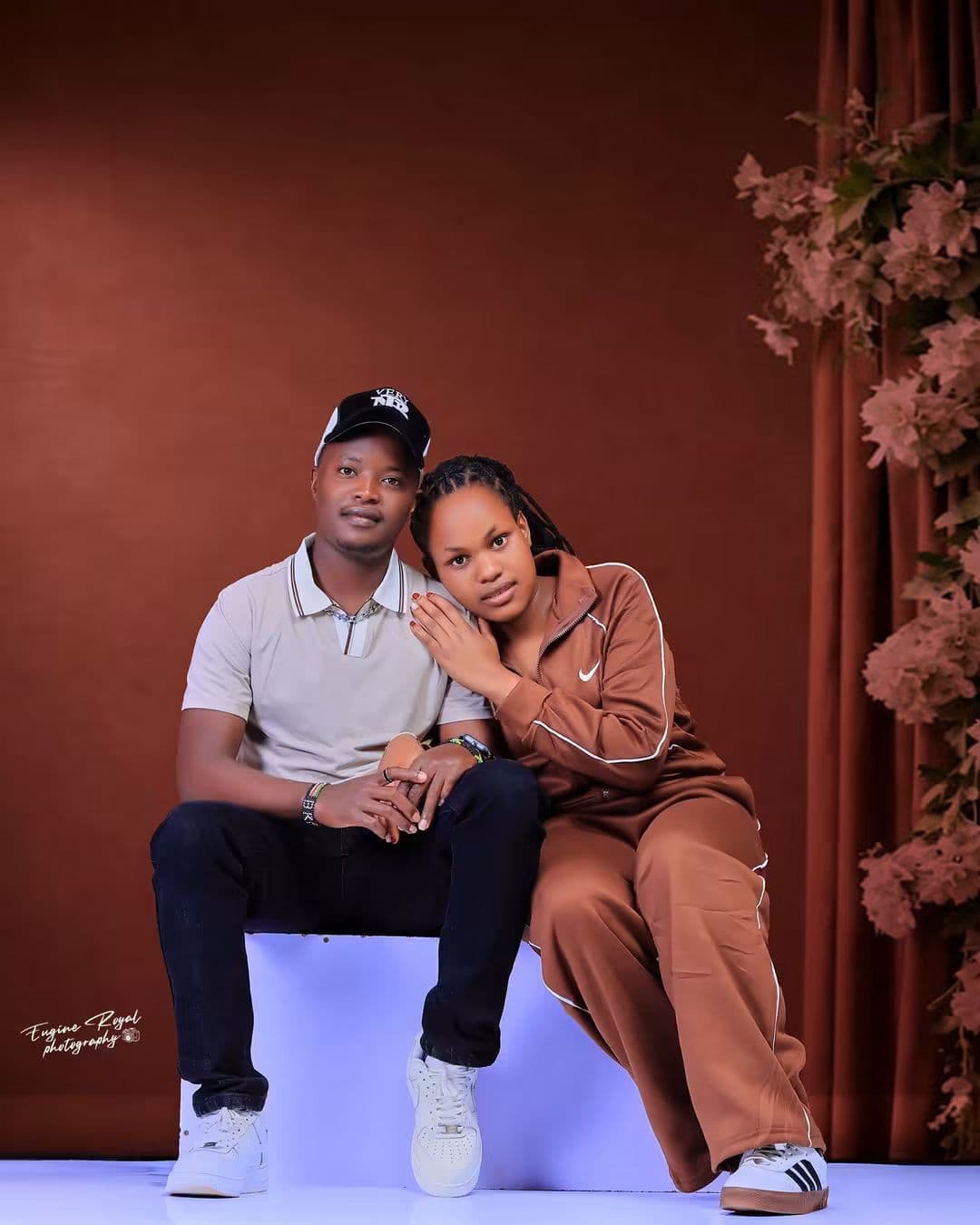 Couple seated close together on a white block against a dusky pink studio set
